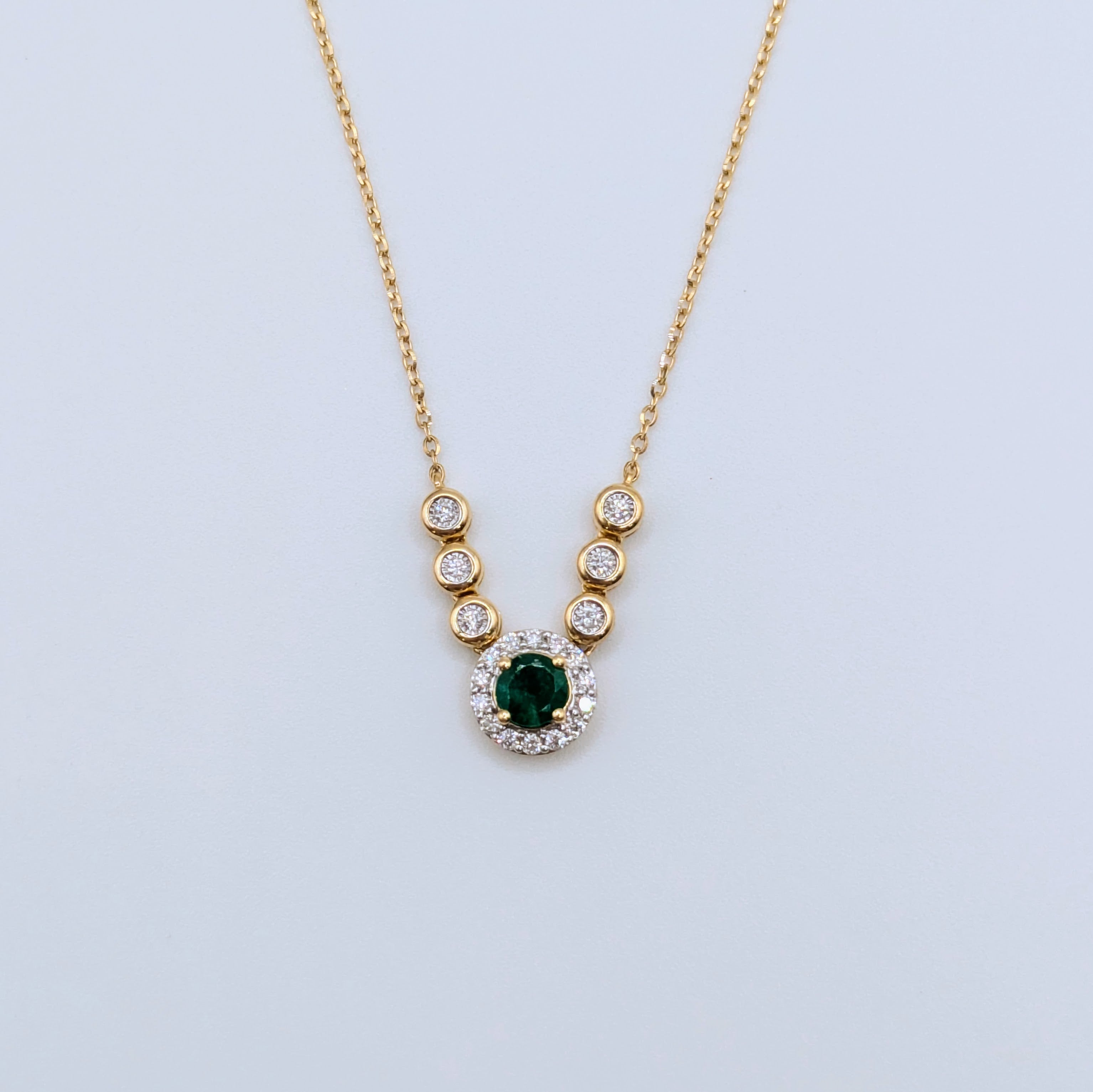 emerald in diamond halo pendant on 18k yellow gold
